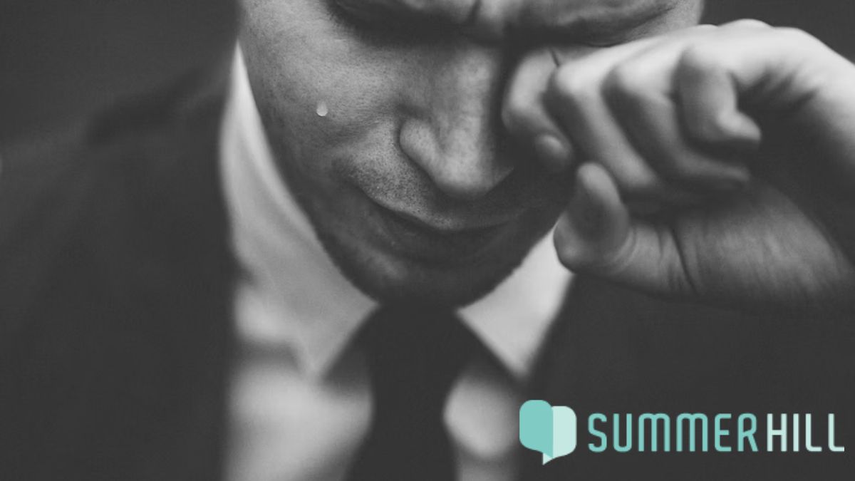 Black and white photo of a man rubbing his eyes in exhaustion, struggling to hold back tears.