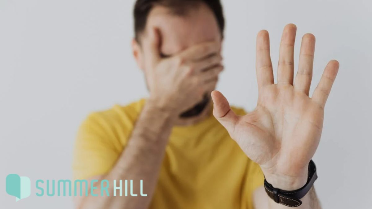 Man in a yellow shirt raising one hand to signal stop while covering his eyes with the other.