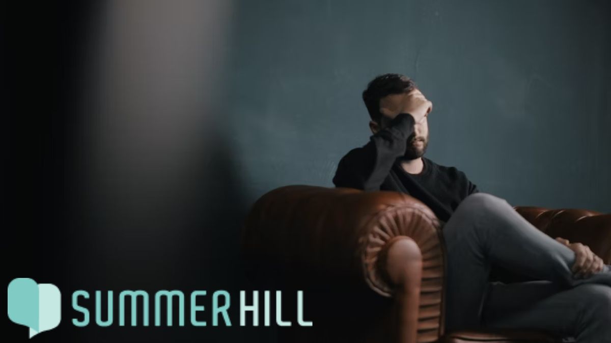 Color photo of a man looking stressed while sitting on a couch at the end of the day, with a tired and reflective expression.