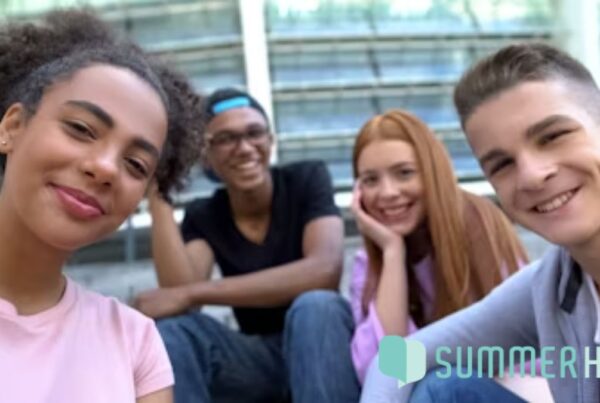 A group of young people sit on concrete stairs outside a building, smiling at the camera in a welcoming display of mental health awareness.