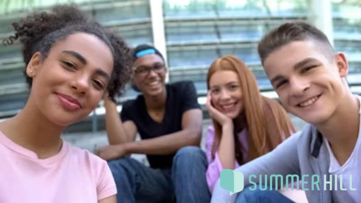 A group of young people sit on concrete stairs outside a building, smiling at the camera in a welcoming display of mental health awareness.