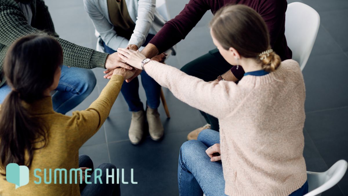 A group of young people place their hands together in a therapy session, symbolizing unity for mental health awareness.