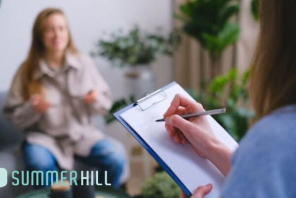A woman receives CBT for bipolar disorder, shown in soft focus while the therapist takes notes during the session.