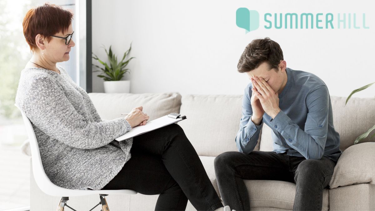 A young man presses his face into his hands, showing emotion during a talk therapy session in CBT for bipolar disorder.