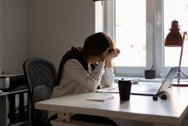 Masking Anxiety: A woman sits in an office with a wide window framing the skyline, her hands covering her face in an act of frustration.