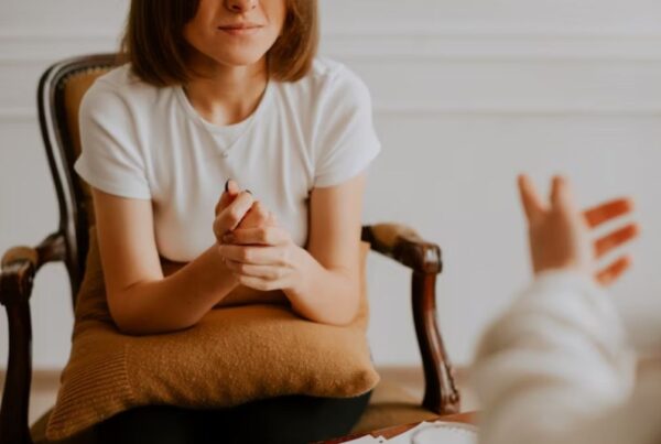 A patient, who has outgrown her current therapist, clasps her hands while talking to her therapist, who gestures with his hands in a brightly lit room. Only their torsos and hands are visible.