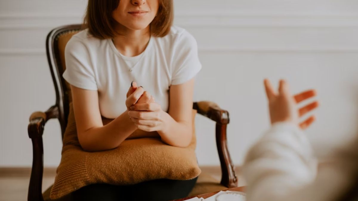A patient, who has outgrown her current therapist, clasps her hands while talking to her therapist, who gestures with his hands in a brightly lit room. Only their torsos and hands are visible.