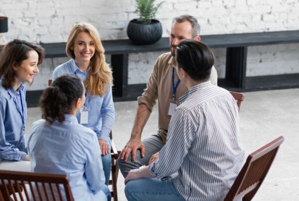 A family of adult members sits together in a circle during therapy, smiling and engaged in open conversation. The atmosphere feels warm, supportive, and full of understanding, capturing the essence of positive family counseling.