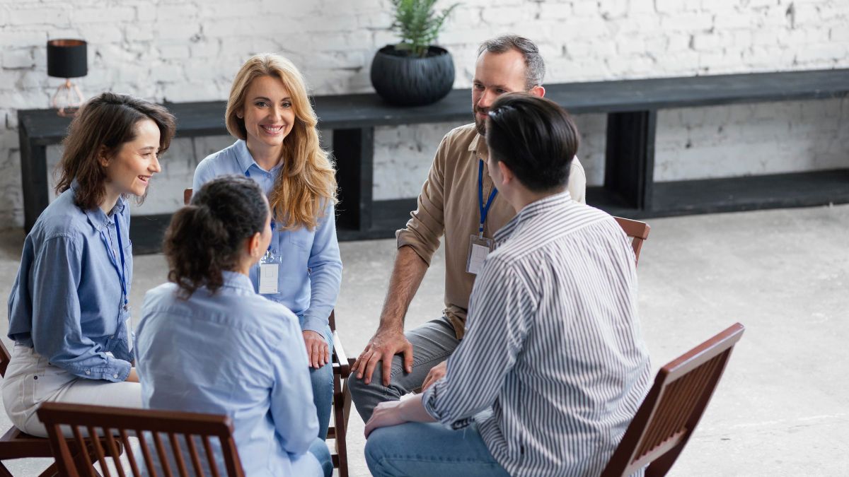 A family of adult members sits together in a circle during therapy, smiling and engaged in open conversation. The atmosphere feels warm, supportive, and full of understanding, capturing the essence of positive family counseling.