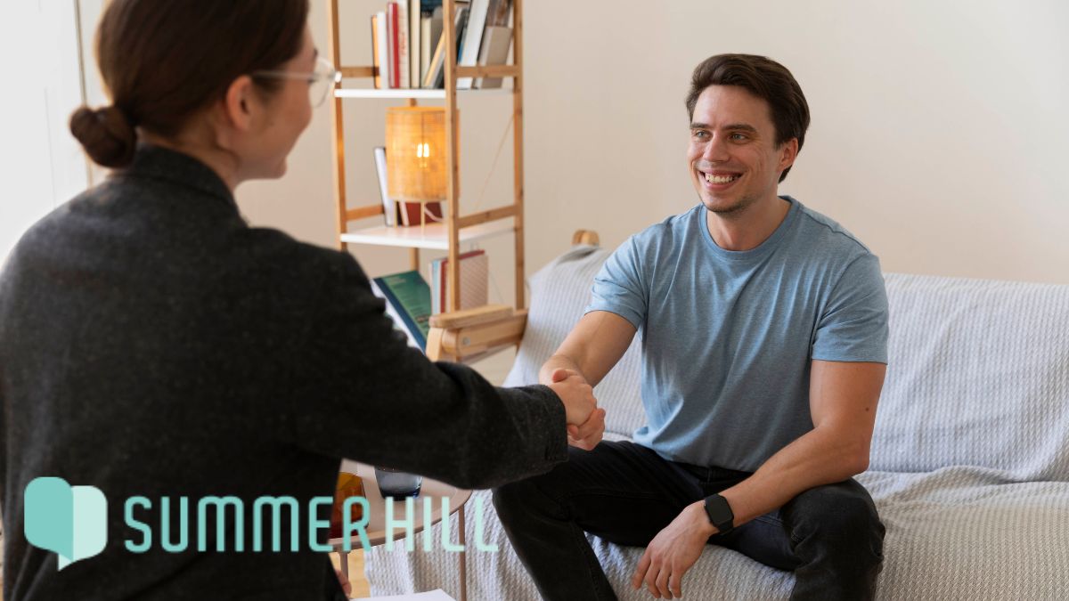 A male patient smiles pleasantly while shaking hands with a therapist during a stress therapy session.
