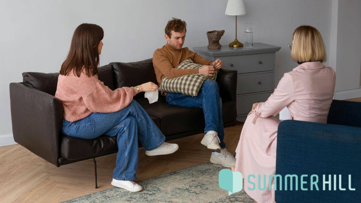 A couple sits together during a family counseling session, engaged in an intense emotional discussion while the therapist listens attentively, fostering understanding and connection.
