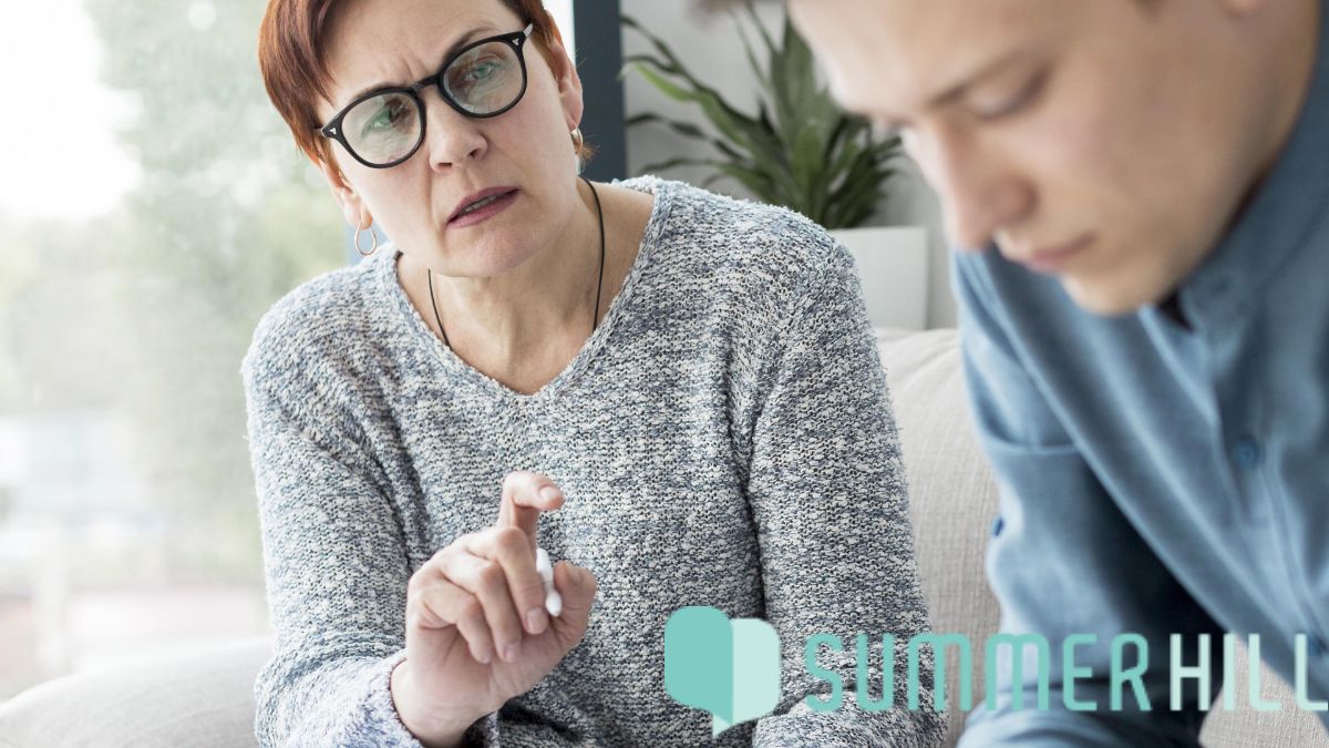 A man with head bowed receives DBT counseling while managing intense emotions.